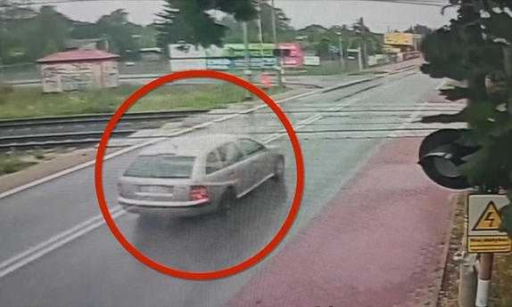 Stopklatka z nagrania przedstawia samochód na przejeździe kolejowym.