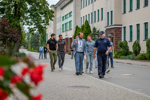 Mężczyźni idą chodnikiem wraz z policjantem.
