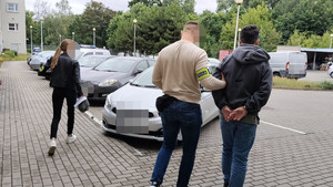 Funkcjonariusz prowadzi zatrzymanego mężczyznę.