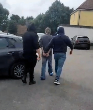 Zatrzymany mężczyzna prowadzony przez policjantów.