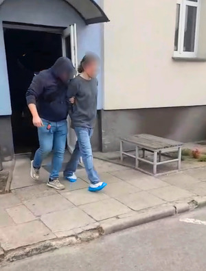Zatrzymany mężczyzna prowadzony przez policjanta.