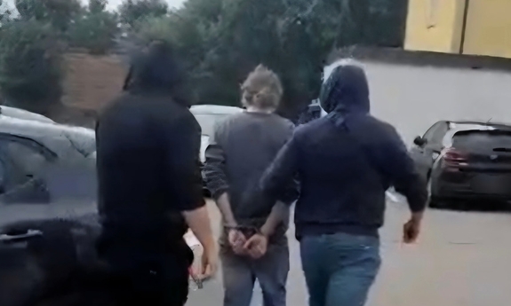 Zatrzymany mężczyzna prowadzony przez policjantów.