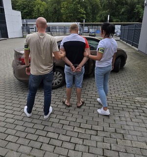 Policjant i policjantka z zatrzymanym mężczyzną.