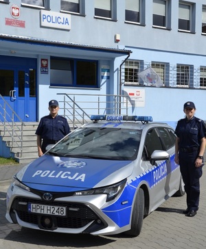 Dwie policjantki przy radiowozie, który zaparkowany jest przed budynkiem Komendy Powiatowej Policji w Szydłowcu.