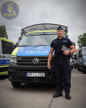 Policjant stoi przed radiowozem.