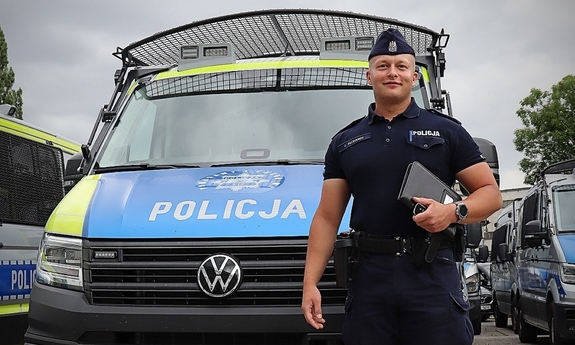 Policjant stoi przed radiowozem.