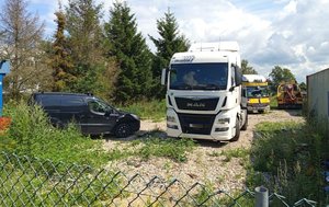 Zaparkowany ciągnik siodłowy - przód, obok stoi auto osobowe, w głębi drugi ciągnik siodłowy.