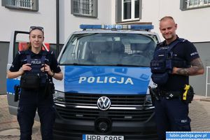 Policjant i policjantka stoją przy radiowozie policyjnym.