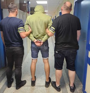 Policjanci stoją z zatrzymanym mężczyzną.