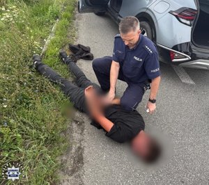 Policjant zakłada kajdanki zatrzymanemu mężczyźnie leżącemu na ziemi.