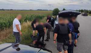 Grupa funkcjonariuszy stoi wokół mężczyzny leżącego na drodze.