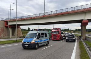 Radiowóz policyjny stoi przed samochodem ciężarowym na drodze. Za nimi samochody stojące w korku.