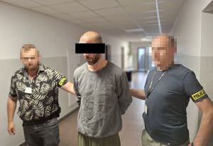 Dwaj funkcjonariusze prowadzą zatrzymanego w kajdankach.