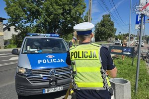 Dwaj funkcjonariusze stoją przy radiowozie zaparkowanym przy ulicy.
