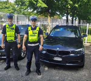 Dwaj policjanci przy nieoznakowanym radiowozie.