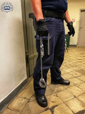 Policjant trzyma w ręku kajdanki zespolone.