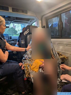 Policjantka siedzi w radiowozie z odnaleziona kobietą, okrytą kocem ratunkowym.