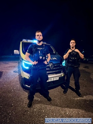 Dwaj policjanci stoją przed radiowozem.