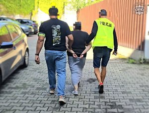 Dwaj policjanci prowadzą zatrzymaną osobę.