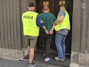 Dwaj policjanci prowadzą zatrzymaną osobę.