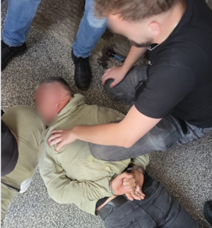 Zatrzymany mężczyzna leży na ziemi. Nad nim stoją zatrzymujący go policjanci.