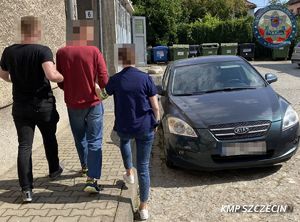 Zatrzymany prowadzony chodnikiem przez dwoje funkcjonariuszy.