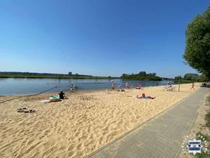 Plaża przy brzegu zbiornika wodnego. Na brzegu odpoczywający ludzie.