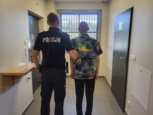 Funkcjonariusz z zatrzymanym mężczyzną na korytarzu.
