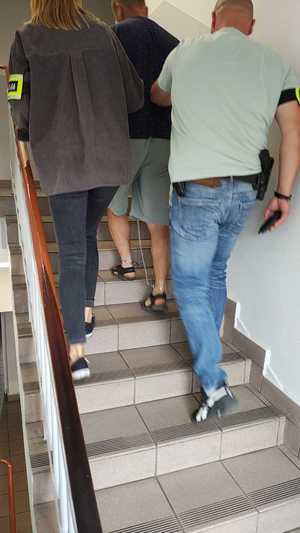 Dwoje funkcjonariuszy prowadzi zatrzymanego mężczyznę.