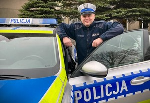 policjant stoi obok radiowozu.
