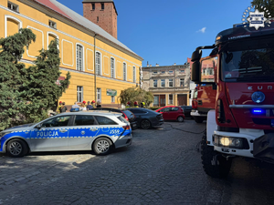 Wozy strażackie i radiowóz przed budynkiem.