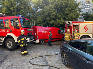 Wozy strażackie i strażacy przed budynkiem.