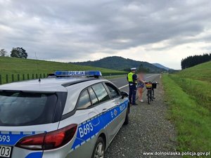 Policjant rozmawia z kobietą trzymającą rower. Obok radiowóz.