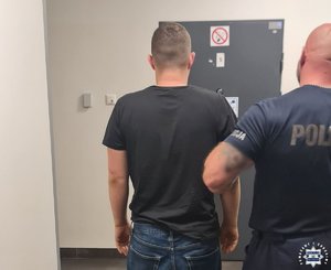Policjant prowadzi zatrzymanego mężczyznę.