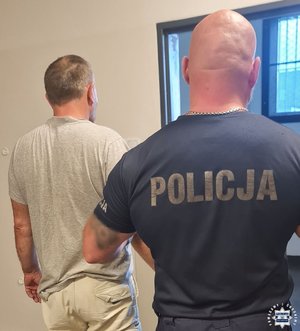 Policjant prowadzi zatrzymanego mężczyznę.