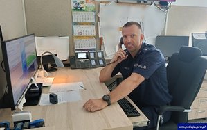 Dyżurny policji siedzi przy biurku i rozmawia przez telefon.