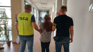 Dwaj funkcjonariusze prowadzą zatrzymanego korytarzem.