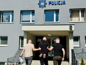 Dwaj funkcjonariusze prowasza zatrzymanego w kierunku budynku komendy Policji.