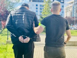 Policjant prowadzi zatrzymanego mężczyznę.