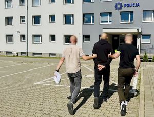 Dwaj funkcjonariusze prowasza zatrzymanego w kierunku budynku komendy Policji.
