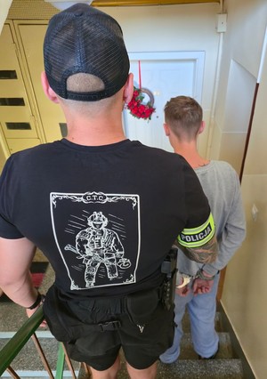 Policjant prowadzi schodami w dół zatrzymanego.