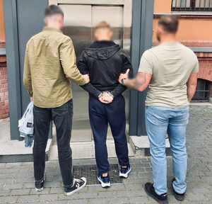 Dwaj funkcjonariusze prowadzą zatrzymanego mężczyznę.