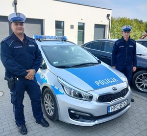 Dwaj policjanci stoją przy radiowozie policyjnym.