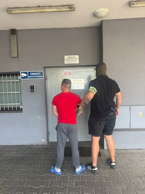 Funkcjonariusz z zatrzymanym przed drzwiami do budynku.