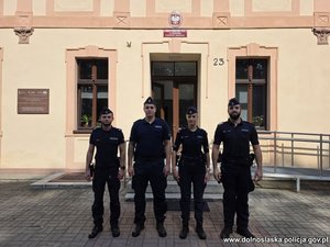Policjantka i trzech policjantów w mundurach przed budynkiem komendy.