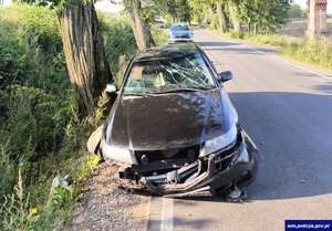 Uszkodzony samochód osobowy na skraju drogi. W głębi zaparkowany radiowóz.