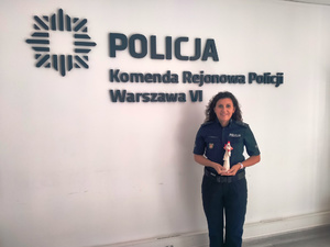 Policjantka stoi na tle ściany z napisem Policja Komenda Rejonowa Policji Warszawa IV.