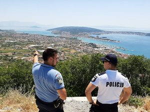Wspólny międzynarodowy  patrol dwóch policjantów rozmawiających na wzniesieniu klifowym,  spoglądających w dal na teren zabudowany z linią przybrzeżną oraz akwenem morskim.