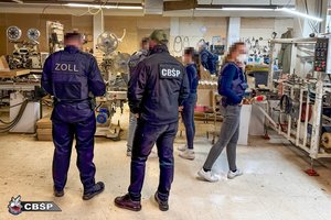 Umundurowani i nieumundurowani policjanci różnych państw podczas działań w pomieszczeniu produkcyjnym.