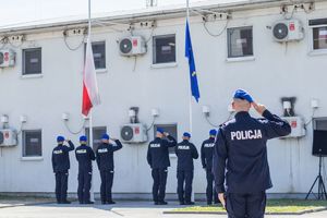 Na zdjęciu budynek, policjanci i dwie flagi na masztach
